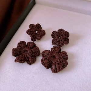 Close-up of brown hand-woven flower drop earrings featuring detailed raffia texture