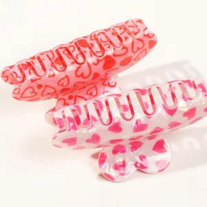 Detail view of pink and red acrylic heart-patterned hair claws on a clean background