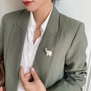 Detail of cute white enamel elephant brooch with gold trim on olive green blazer