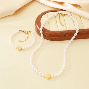 Elegant pearl necklace and bracelet set with golden heart pendants on silk fabric