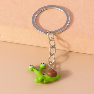 Close-up of a cute green cartoon snail keychain with silver metal ring on a warm background