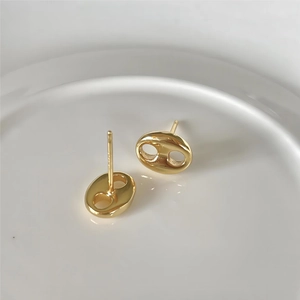 Close-up of golden coffee bean link earrings in a minimalist ceramic dish setting