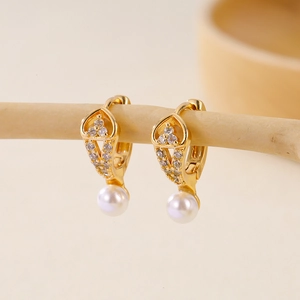 Macro shot of gold-plated pearl drop earrings with white zircon accents on wood display