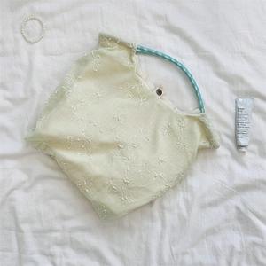 Detail of floral embroidery and braided rope handle on light green canvas tote bag
