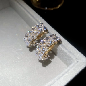Macro detail of gold C-shape hoop earrings with double-row cubic zirconia in a jewelry box