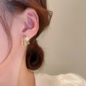 Close-up of elegant gold multi-layered earrings with zircon stones and a white pearl on a model