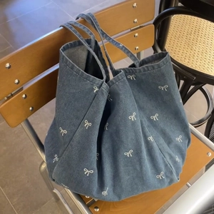 Blue denim tote bag with white bow print hanging on a wooden chair, casual style