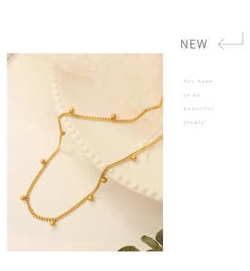 Detailed close-up of a delicate gold beaded chain necklace on a white lace ceramic plate