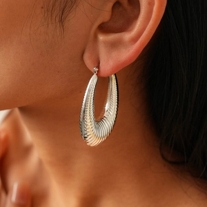 Macro detail of large silver oval hoop earring with elegant horizontal textured stripes