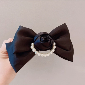Macro shot of black satin bow hair clip with rose flower and pearl center detail