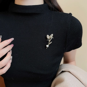 Detail of 14K gold plated tulip brooch with cubic zirconia and pearl on black sweater