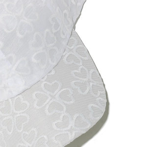 Dettaglio del ricamo in pizzo bianco con motivi a quadrifoglio di cuori su un cappello