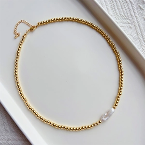 Minimalist gold beaded necklace with a white baroque pearl pendant on a tray