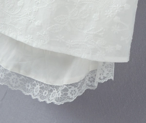 Détail de la robe blanche avec broderie florale et bordure en dentelle festonnée délicate