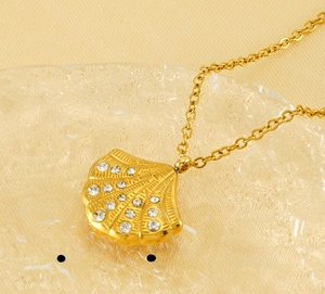 Macro shot of 18K gold shell pendant featuring inlaid diamonds and polished steel finish
