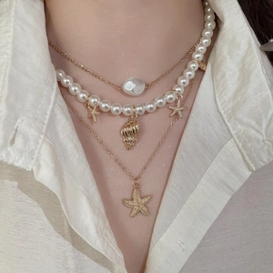 Three-layer gold starfish and pearl shell pendant necklace worn on neck over white shirt