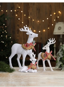 Three white Christmas reindeer figurines with red scarves and bells in a festive setting