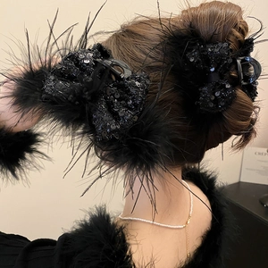 Detailed back view of a large black sequin bow hair claw clip with plush feathers on a bun