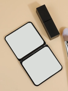 Close-up of black folding pocket mirror with dual mirrors beside a lipstick on warm surface