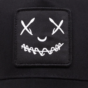 Close-up of black mesh cap with white embroidered devil smile face patch in street style