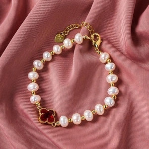 Detail view of pearl bracelet with red clover charm and 925 silver tag on pink fabric