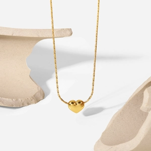Detailed view of 18K gold plated 3D heart pendant on a stone platform with a white backdrop