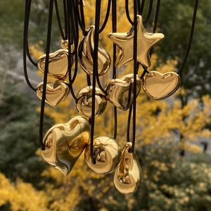 Close-up of golden heart and star pendants on black cords with a blurred autumn background