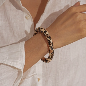Close-up of model wearing a leopard print faux leather open bangle over a white shirt