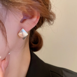 Gros plan d'une boucle d'oreille losange argentée avec texture mate sur un mannequin