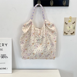Detail of floral canvas tote bag with purple plaid handles and brand woven label