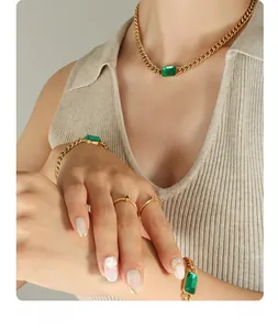Close-up of gold Cuban chain necklace and bracelet set with emerald green gemstones