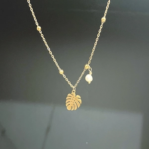 Detail shot of gold monstera leaf pendant with white pearl on beaded chain necklace