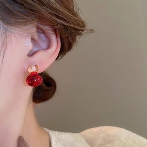 Close-up of double-layered amber and dark red resin ball stud earrings on a model