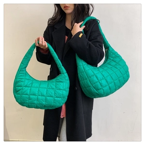 Detailed view of green quilted nylon shoulder bags in two sizes held by a model