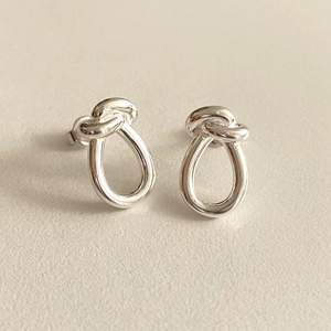 Detailed close-up of S925 sterling silver knot stud earrings on soft warm background