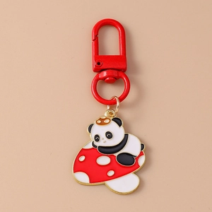 Detail of red enamel mushroom and panda keychain charm with golden metal accents