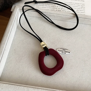 Detail of red flocked resin ring pendant with golden metal clasp on black cord necklace
