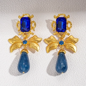 Macro detail of vintage gold bow earrings with sapphire blue stones and marble teardrops