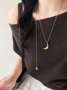 Detail of a gold croissant pendant on a thin silver chain worn over a brown sweater