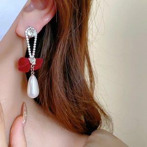 Close-up of pearl drop earrings with red bow and crystal accents on a model