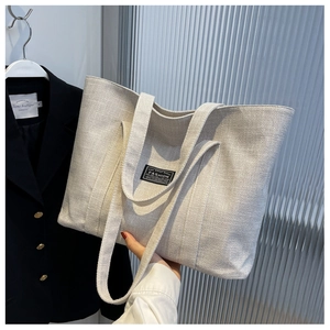 Detail of oat-colored tote bag in textured linen fabric with Fashion label accent
