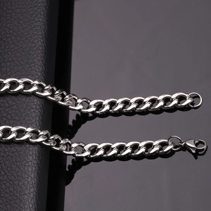 Macro shot of silver stainless steel Cuban link chain on a reflective black surface