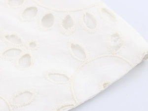 Detailed macro view of white cotton fabric featuring intricate floral eyelet embroidery