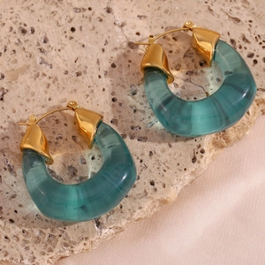 Macro detail of U-shaped green acrylic earrings with gold finish on travertine stone