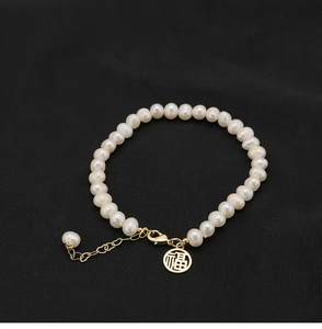 Macro detail of natural pearl bracelet with golden Fu pendant on black fabric