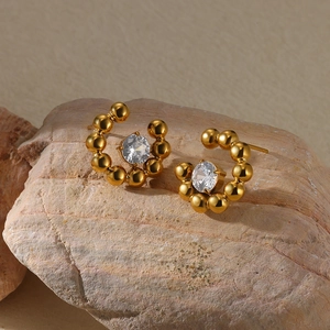 Close-up of gold-plated beaded hoop earrings with central clear zircon on a textured rock