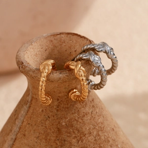 Detailed view of twisted gold and silver hoop earrings on a vintage ceramic bottle