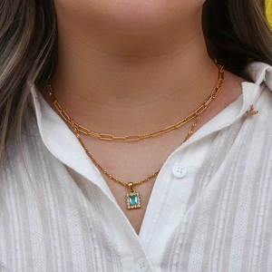 Double-layer gold necklace featuring a rectangular blue gemstone pendant on a model