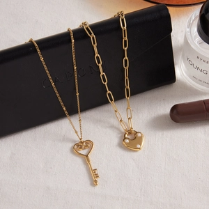 Colliers luxueux en acier inoxydable doré avec pendentifs cœur et clé sur fond élégant