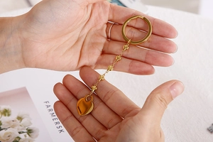 Detail of a golden metal keychain with heart pendants held in hand over a magazine